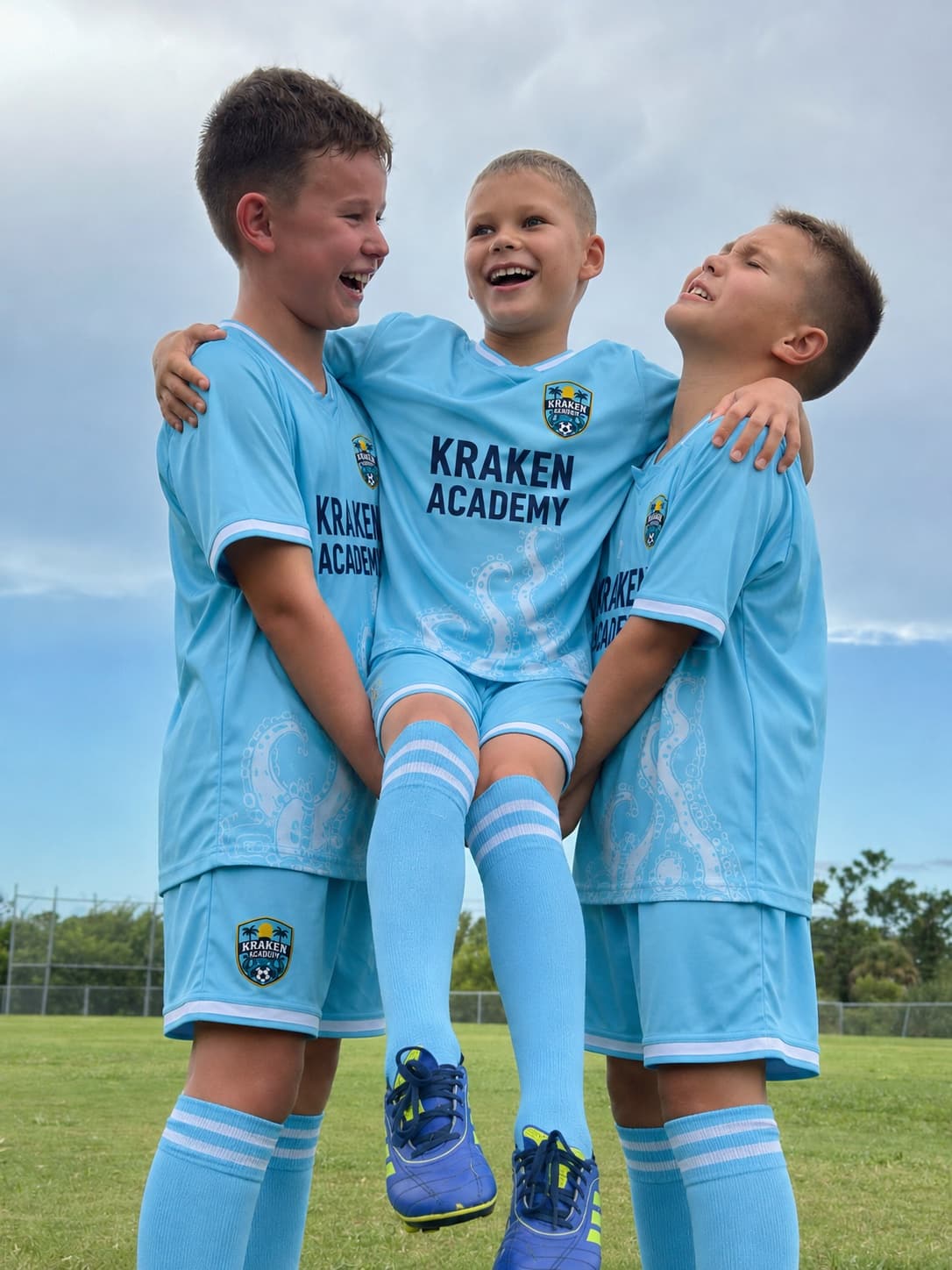 Three young Kraken Academy players laughing together, one lifted by the other two