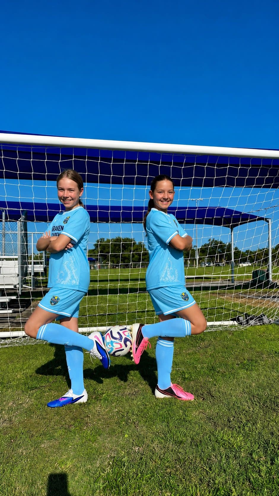 Two Kraken Academy players standing back to back in front of a goal, a ball held between their raised feet
