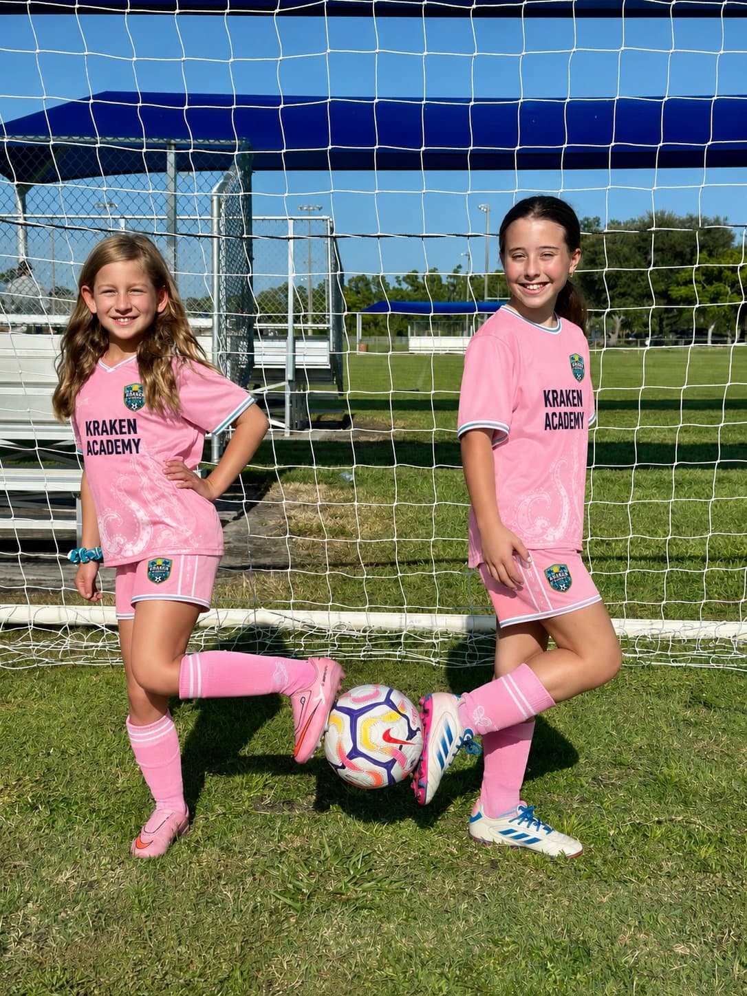 Two Kraken Academy players in the pink kit standing in the goalmouth, one with a foot resting on the ball