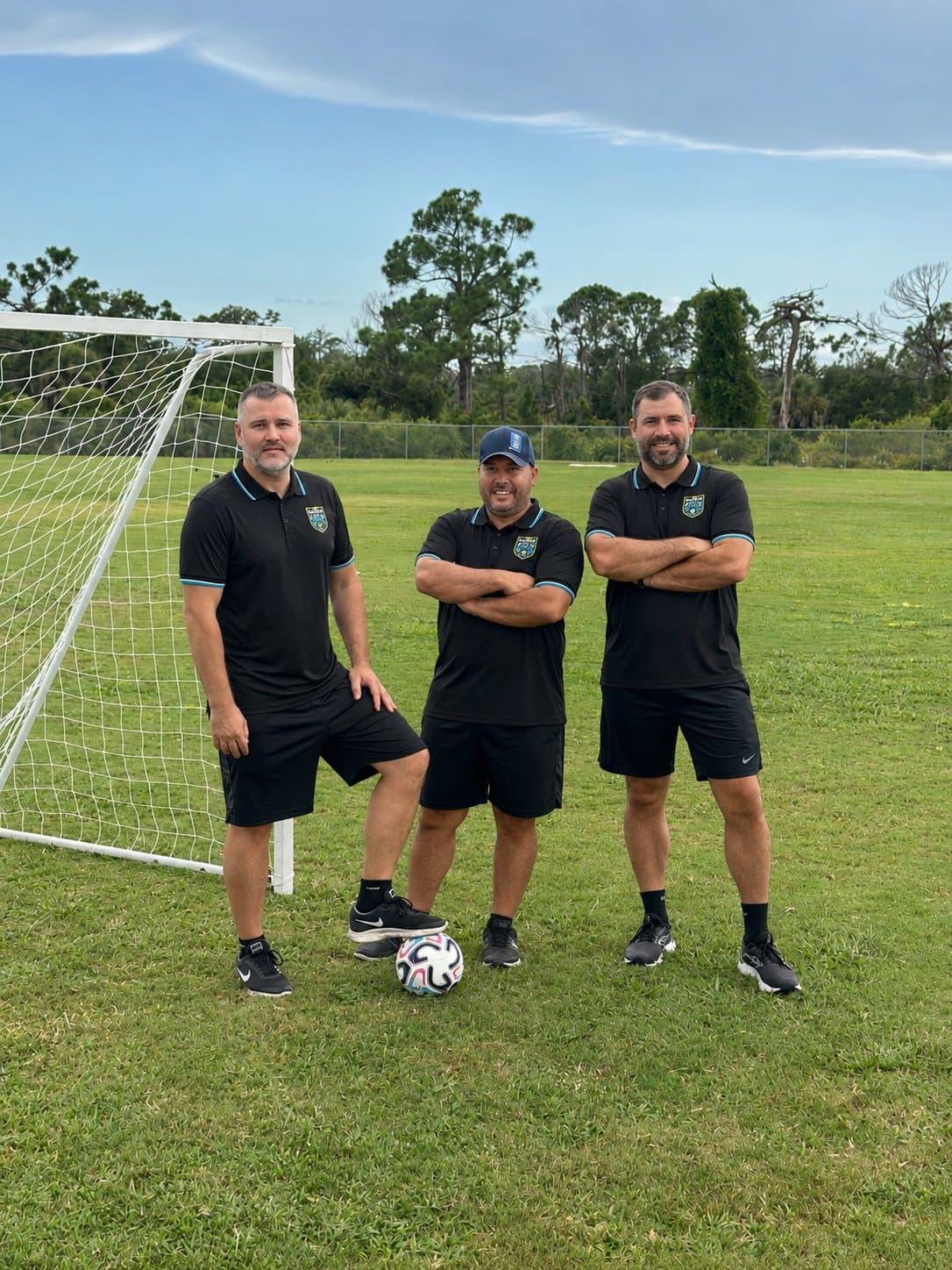 Three Kraken Academy coaches standing beside a goal on the pitch, a ball on the grass in front of them