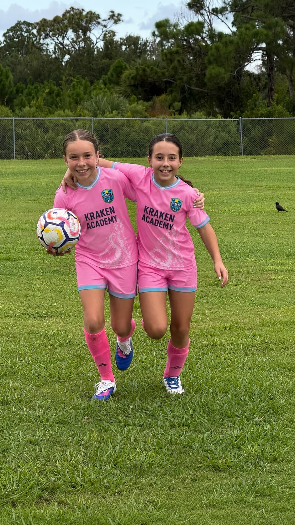 Two Kraken Academy players walking arm in arm across the pitch with a ball