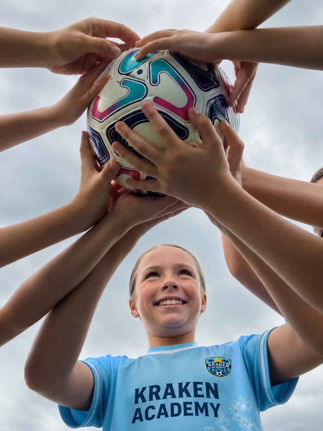 Kraken Academy players reaching in together to hold a ball above them, one player looking up