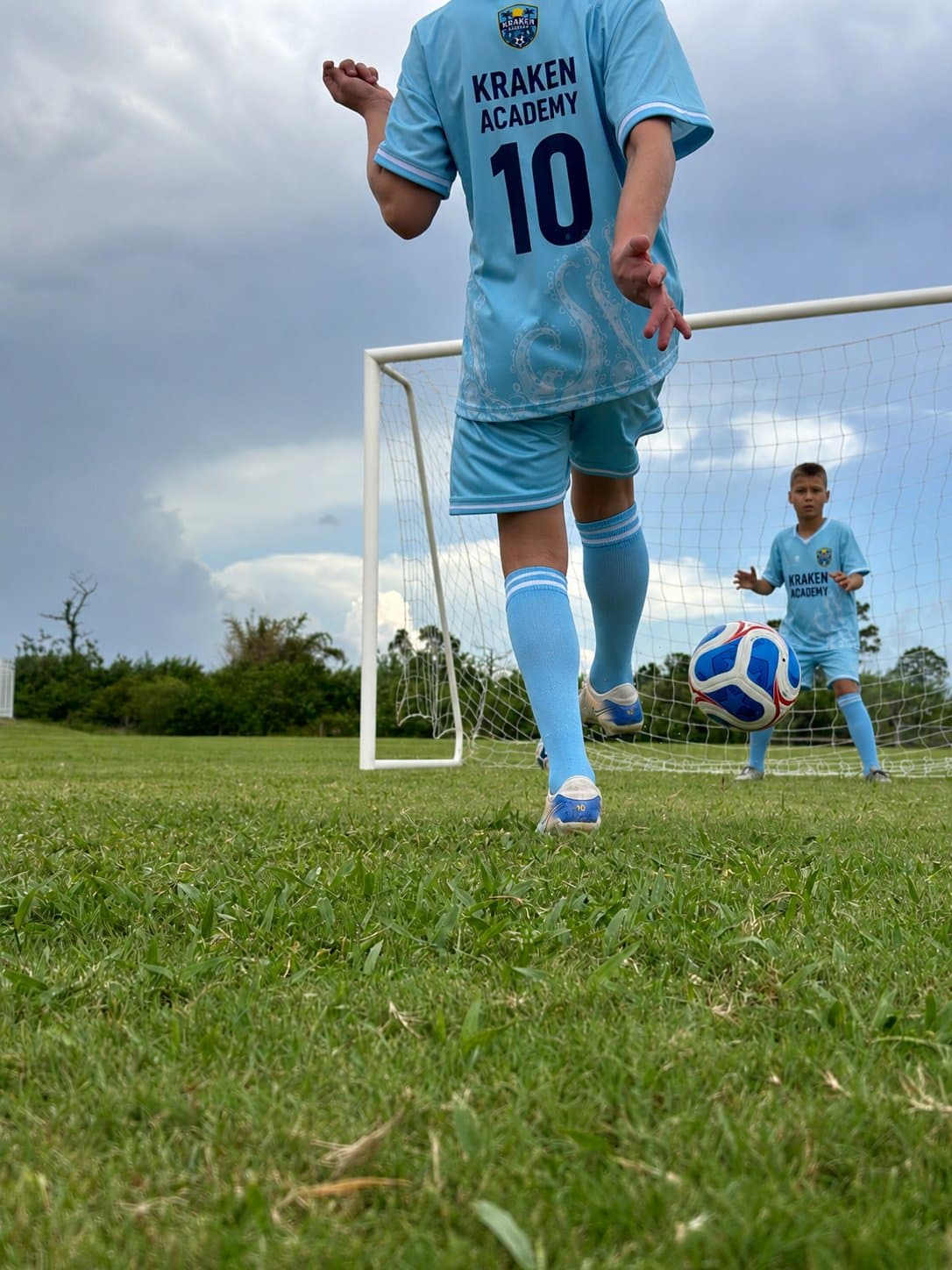A Kraken Academy player in the number 10 shirt walking a ball towards the goal, where another player waits