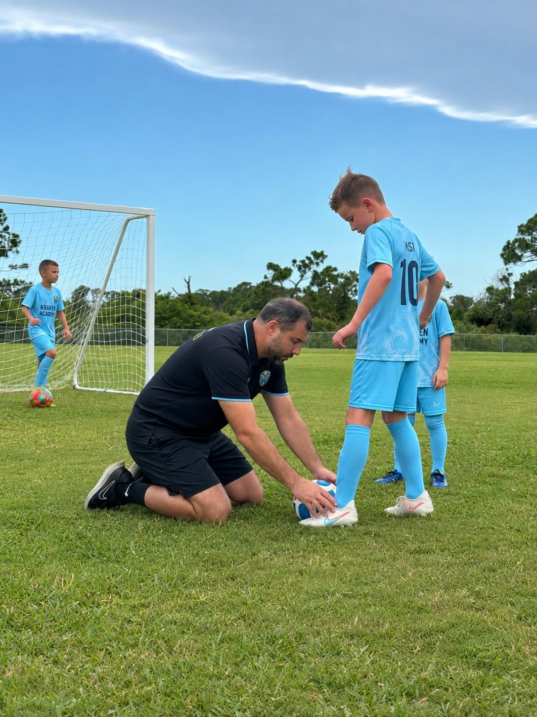 A Kraken Academy coach kneeling to show a young player how to place the ball