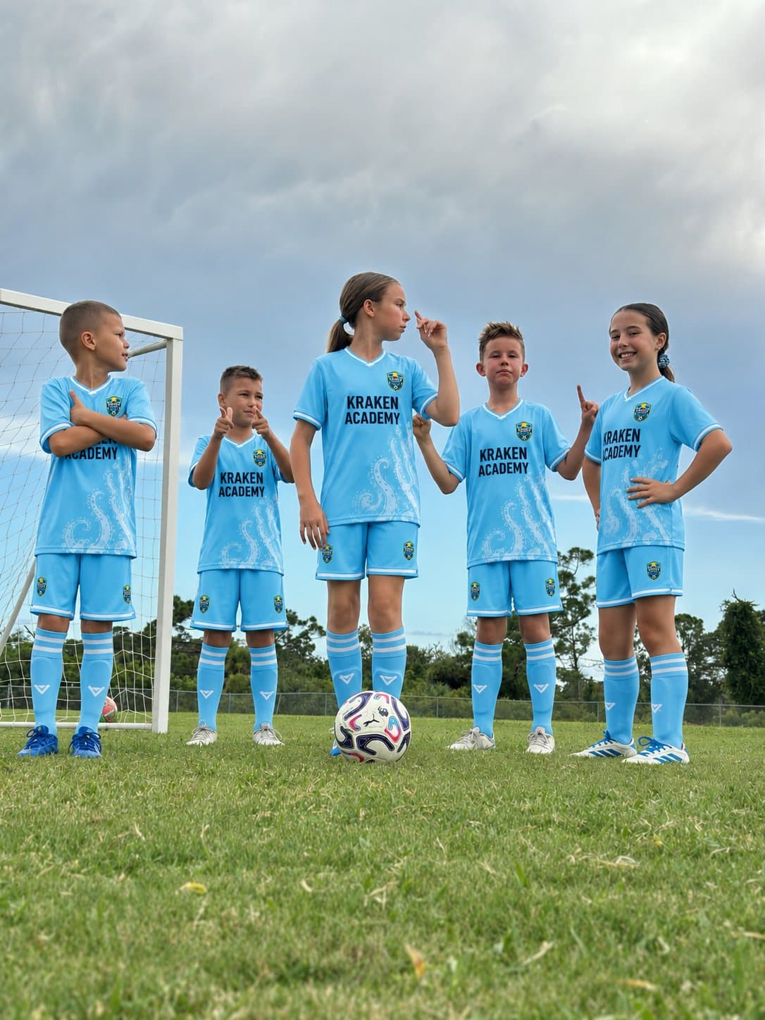 Five Kraken Academy players standing in a line in front of a goal, a ball on the grass at their feet