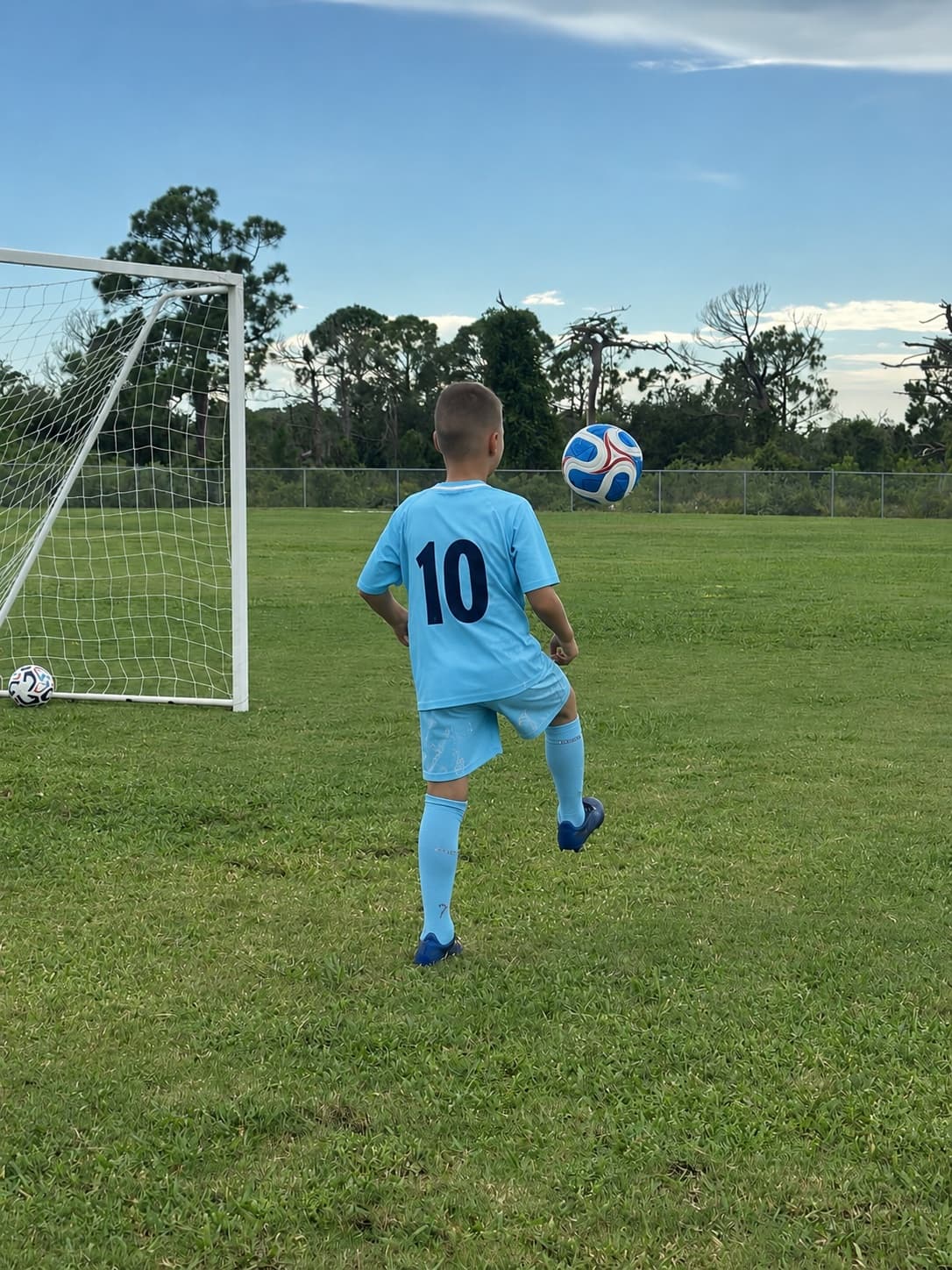A Kraken Academy player alone on an open pitch, watching the ball drop in front of an empty goal