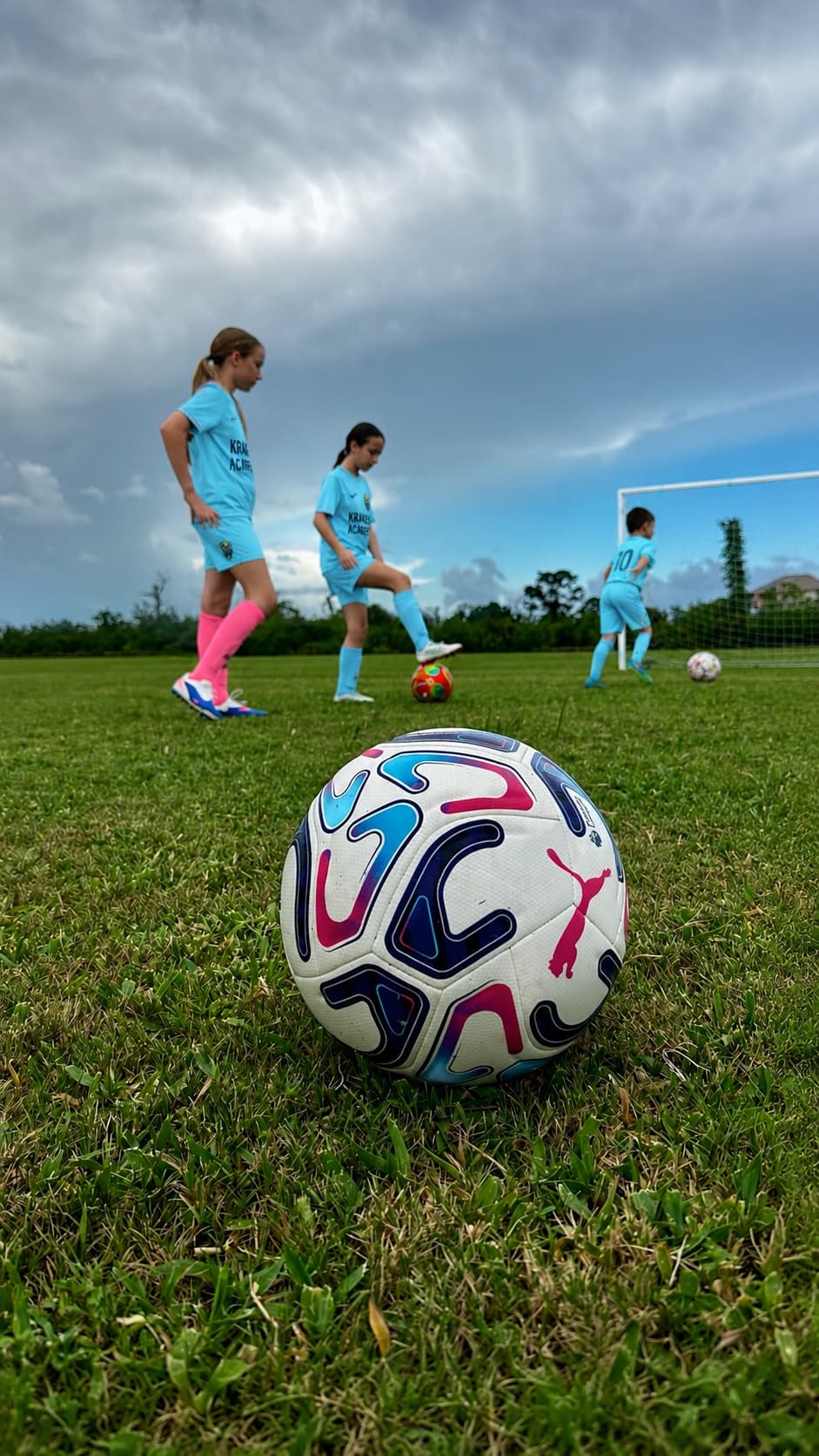 A match ball resting on the grass with Kraken Academy players training behind it