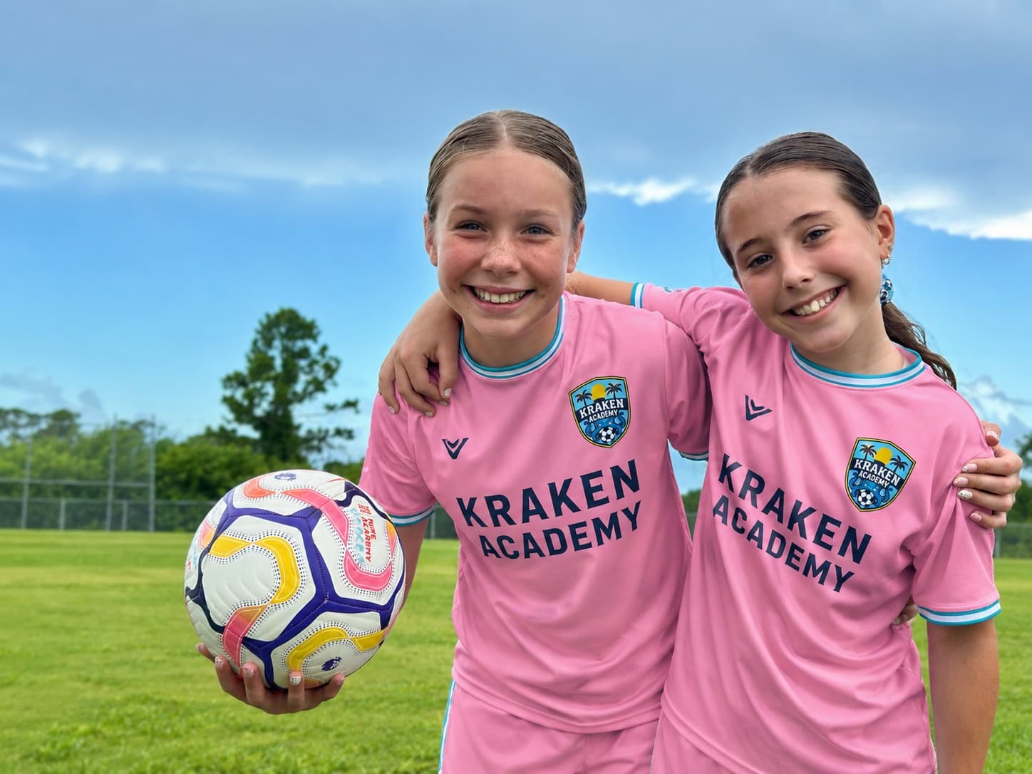 Two Kraken Academy players in the pink kit, arm in arm, one holding a ball